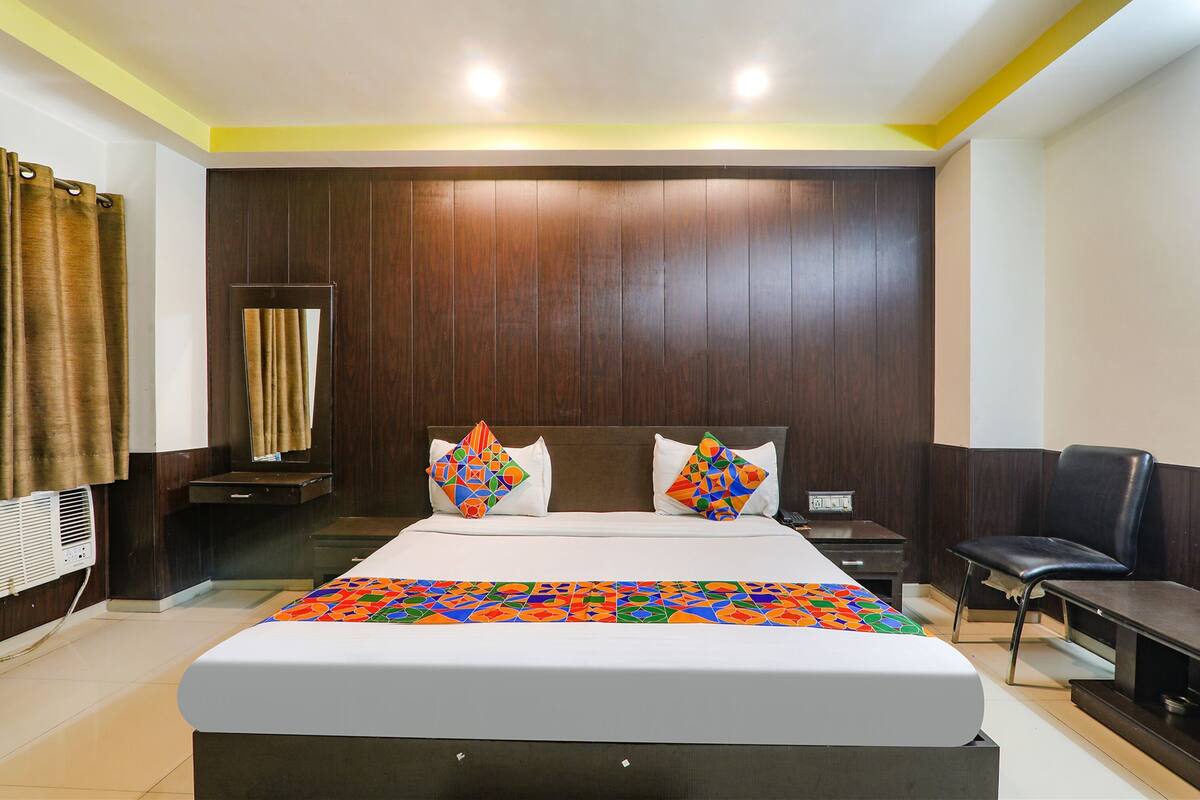 A hotel room with a large bed, a bedside table, a chair, and a mirror.