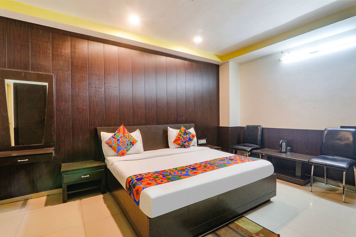 A hotel room with a large bed, a bedside table, a chair, a desk, and a television.