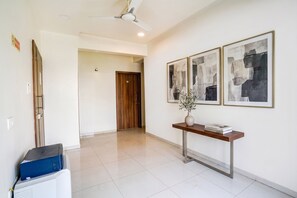 A hotel hallway with a ceiling fan, a wooden door, a console table with a vase and books, and abstract art on the wall. - FabHotel 24 Baner - Nr. MCF Camp (Pune)