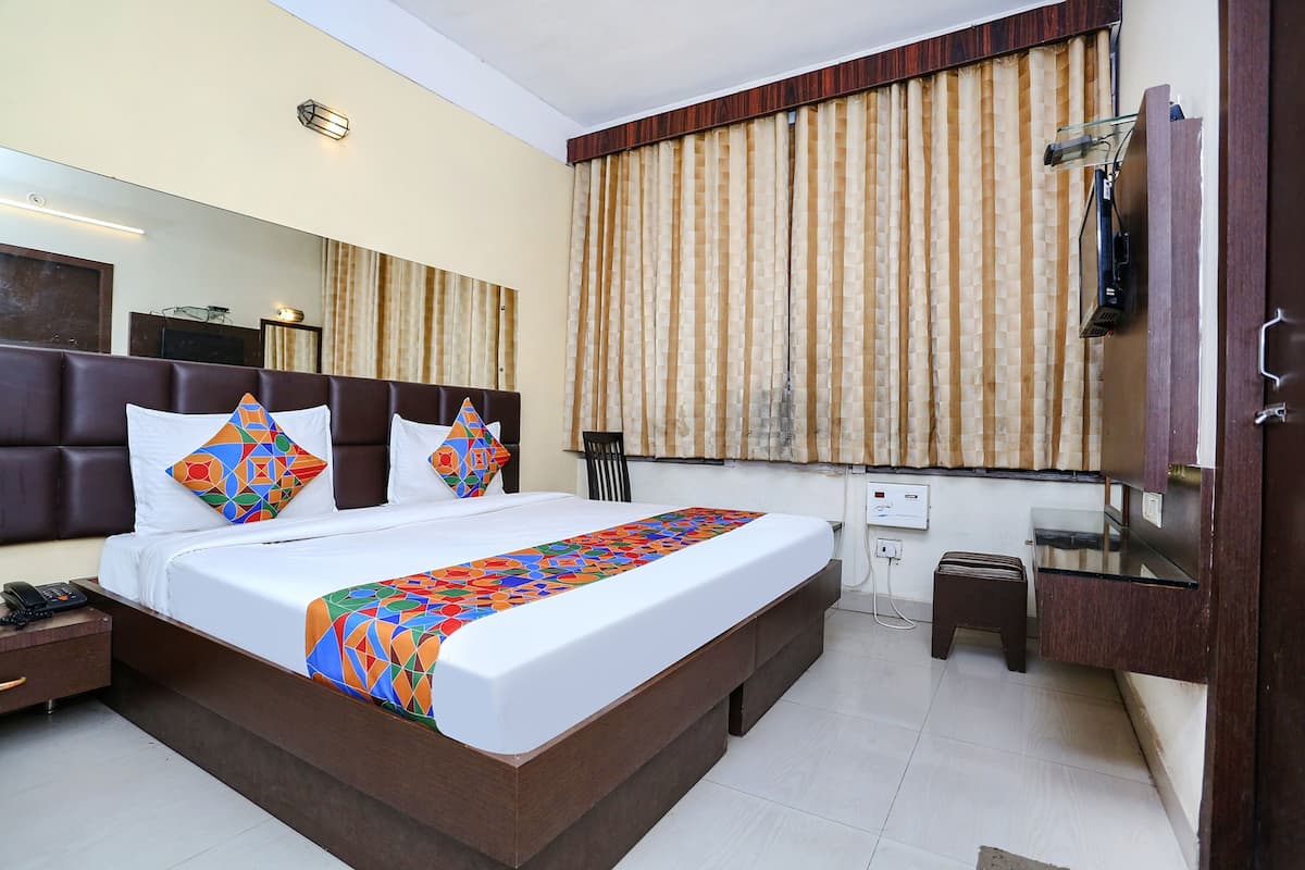 Habitación de hotel con una cama grande, un taburete pequeño, un escritorio, un espejo y una ventana con cortinas.