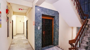 Ein Korridor mit Marmorboden, der zu einer Tür mit einem Metallgitter führt. Rechts ist eine Treppe mit hölzernen Geländern zu sehen.