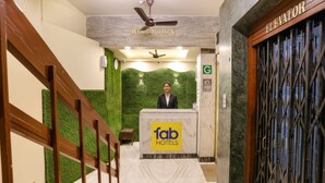 Ein Empfangsbereich mit einer Rezeption mit dem Schild "fab hotels", einer grünen Wand, einem Deckenventilator und einer Treppe mit Holzhandläufen.