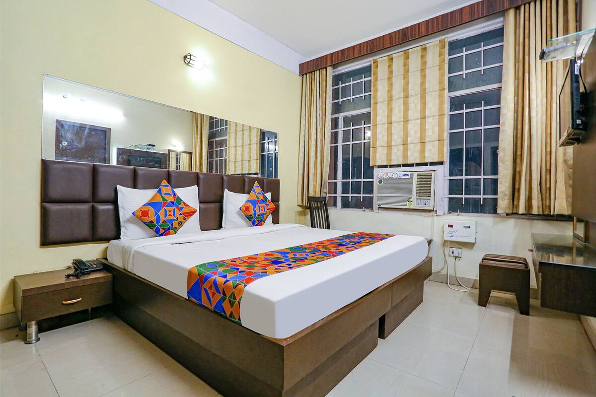 Una habitación de hotel con una cama grande, una mesita de noche, un espejo, una ventana con cortinas y un equipo de aire acondicionado.