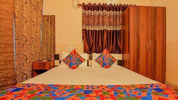 Une chambre à coucher avec un lit, deux oreillers, une armoire en bois et des rideaux à motifs.