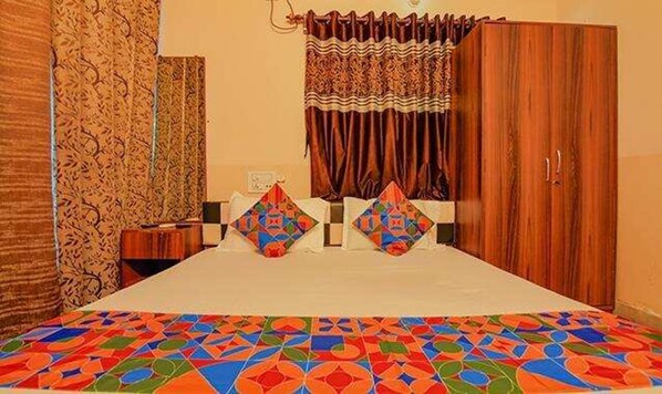 Un dormitorio con una cama, dos almohadas, un armario de madera y cortinas estampadas.