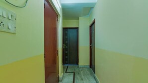 Un couloir étroit, avec une porte en bois au fond, un interrupteur sur le mur et un sol carrelé.