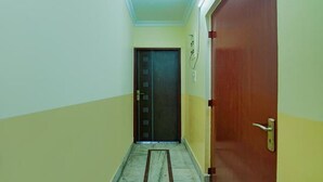 Un couloir étroit, avec une porte en bois sur la droite et une porte noire au fond.