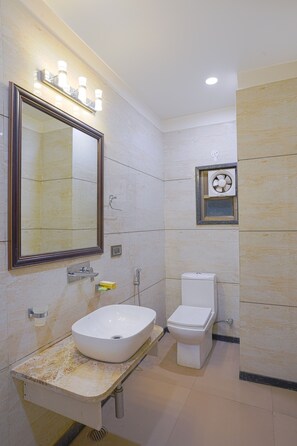 Une salle de bain avec un grand miroir, un lavabo, des toilettes et un ventilateur d’extraction.