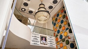 A hotel interior with a chandelier, a staircase, and a wall with circular patterns.