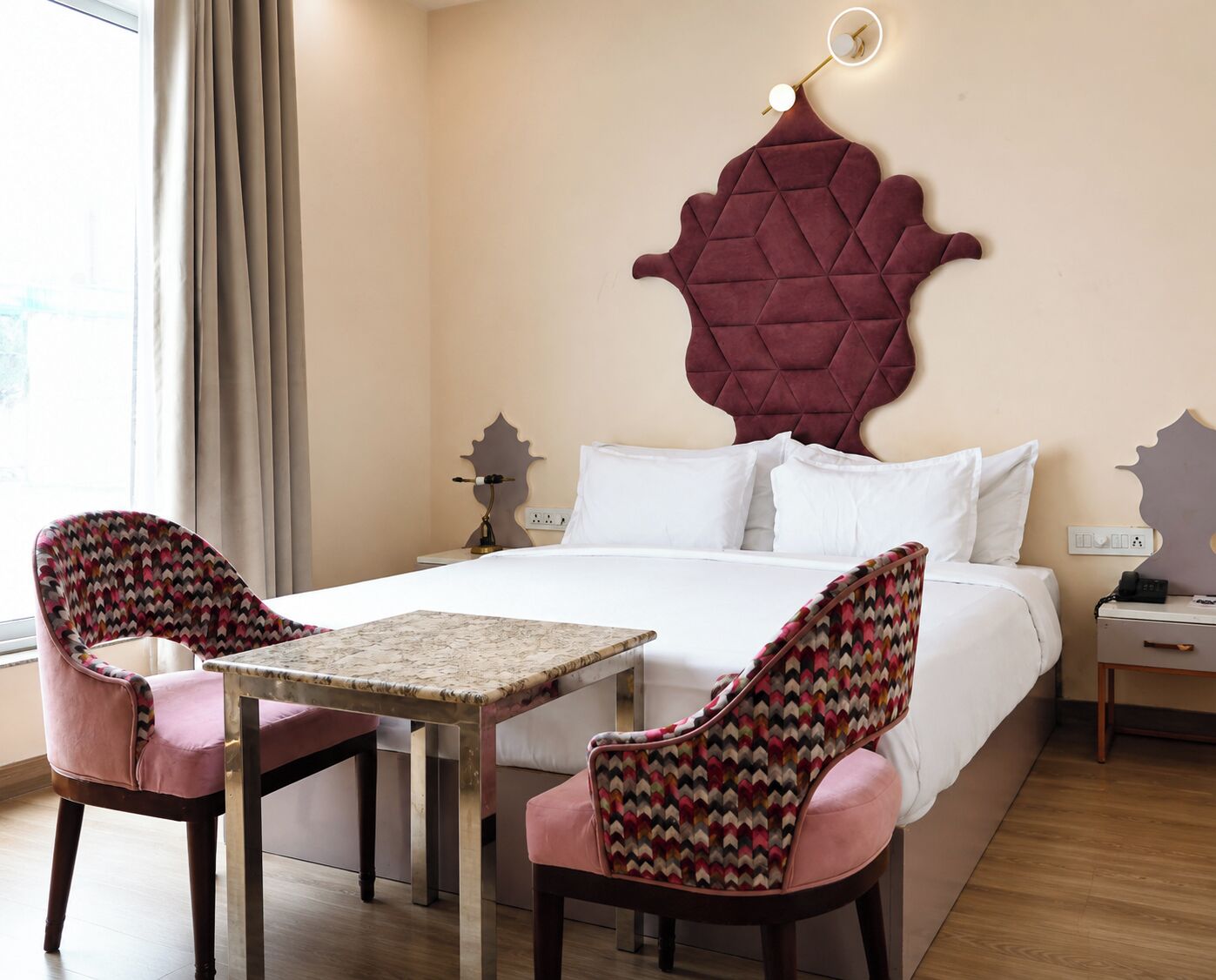 A hotel room with a bed, two chairs, a table, and a wall-mounted light fixture.