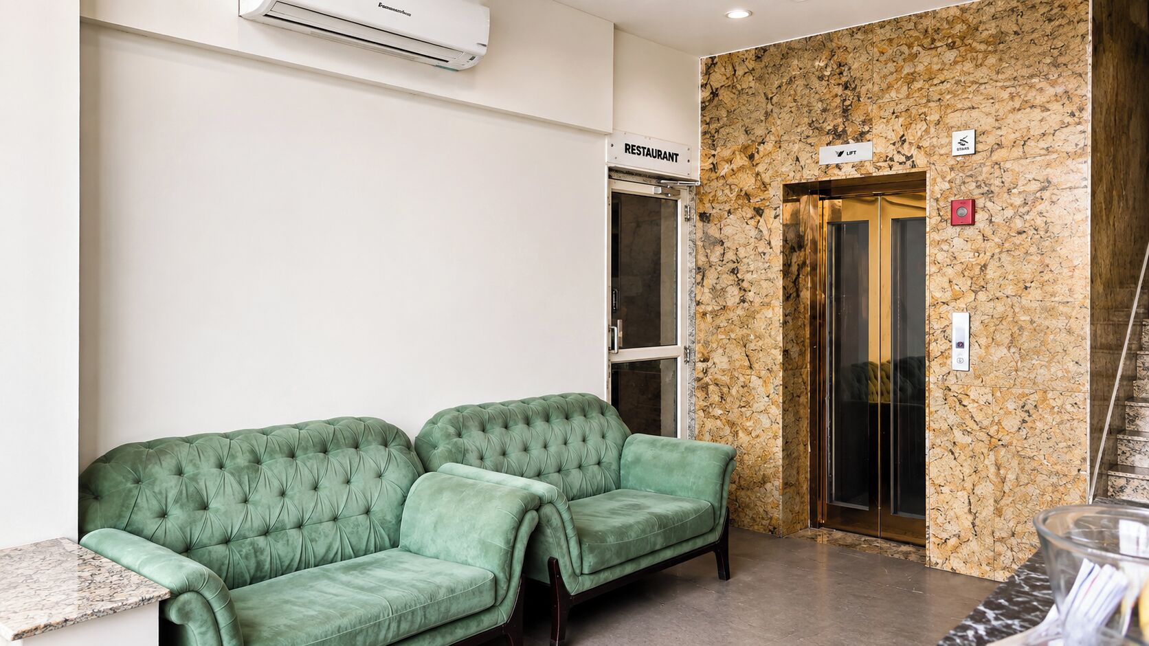 A lobby with a green sofa, a restaurant sign, an elevator, and a marble wall.