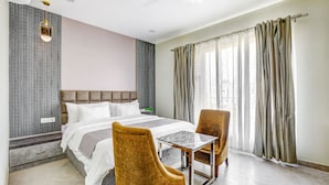 A hotel room with a bed, two chairs, a small table, a ceiling fan, and a window with curtains.