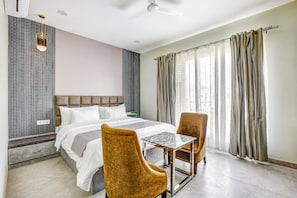 Ein Hotelzimmer mit Bett, zwei Stühlen, einem kleinen Tisch, einem Deckenventilator und einem Fenster mit Vorhängen.