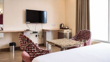 A hotel room with a bed, a desk, a television, and two patterned chairs.