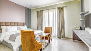A hotel room with a bed, two chairs, a small table, a TV, and a window with curtains.