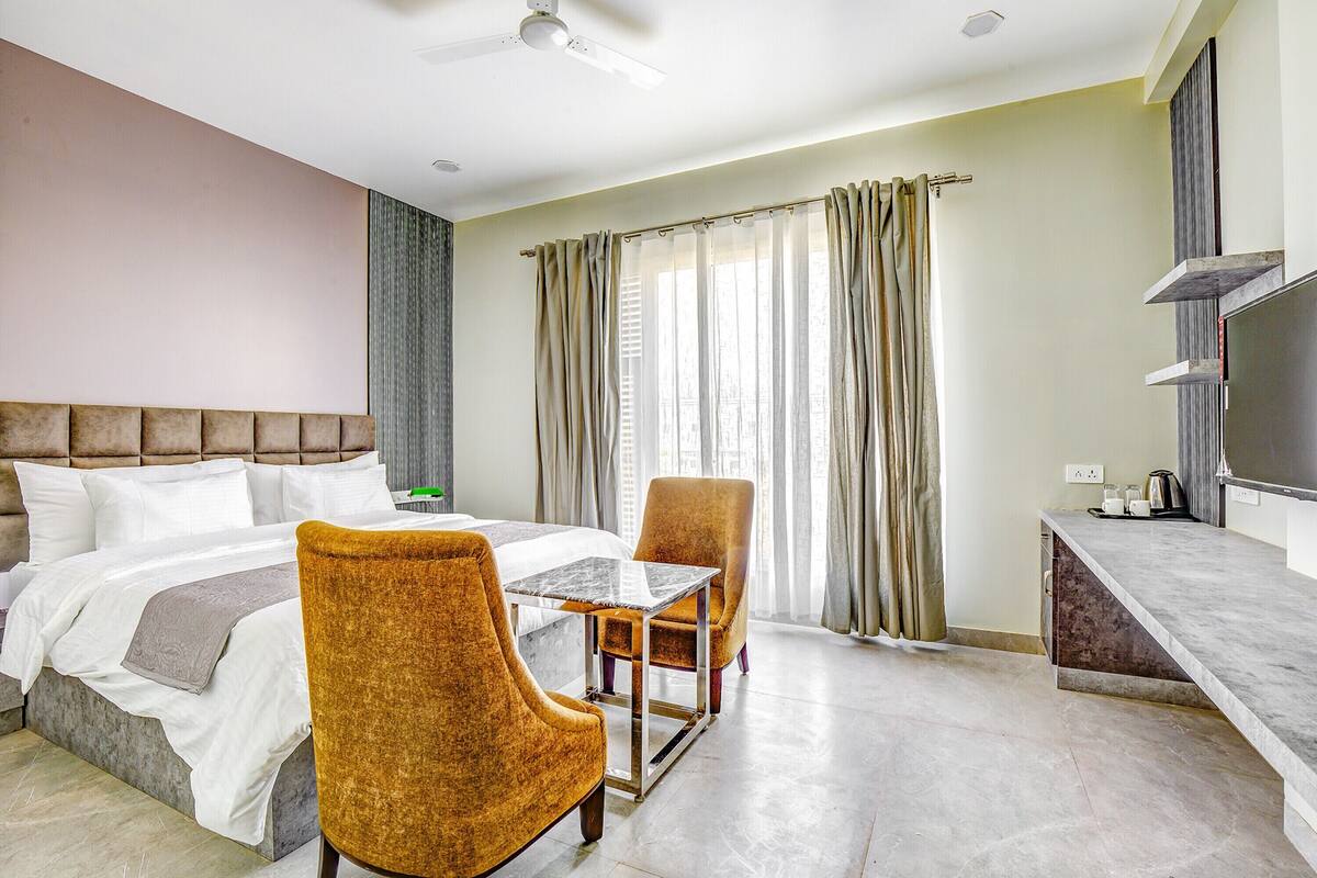 Hotelkamer met een bed, twee stoelen, een tafel, een televisie en een raam met gordijnen.