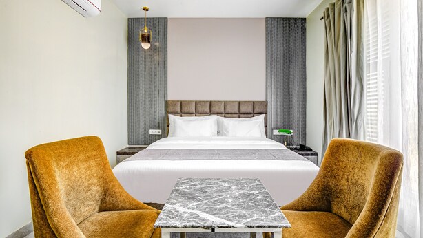 A hotel room with a large bed, two armchairs, a small table, and a nightstand.