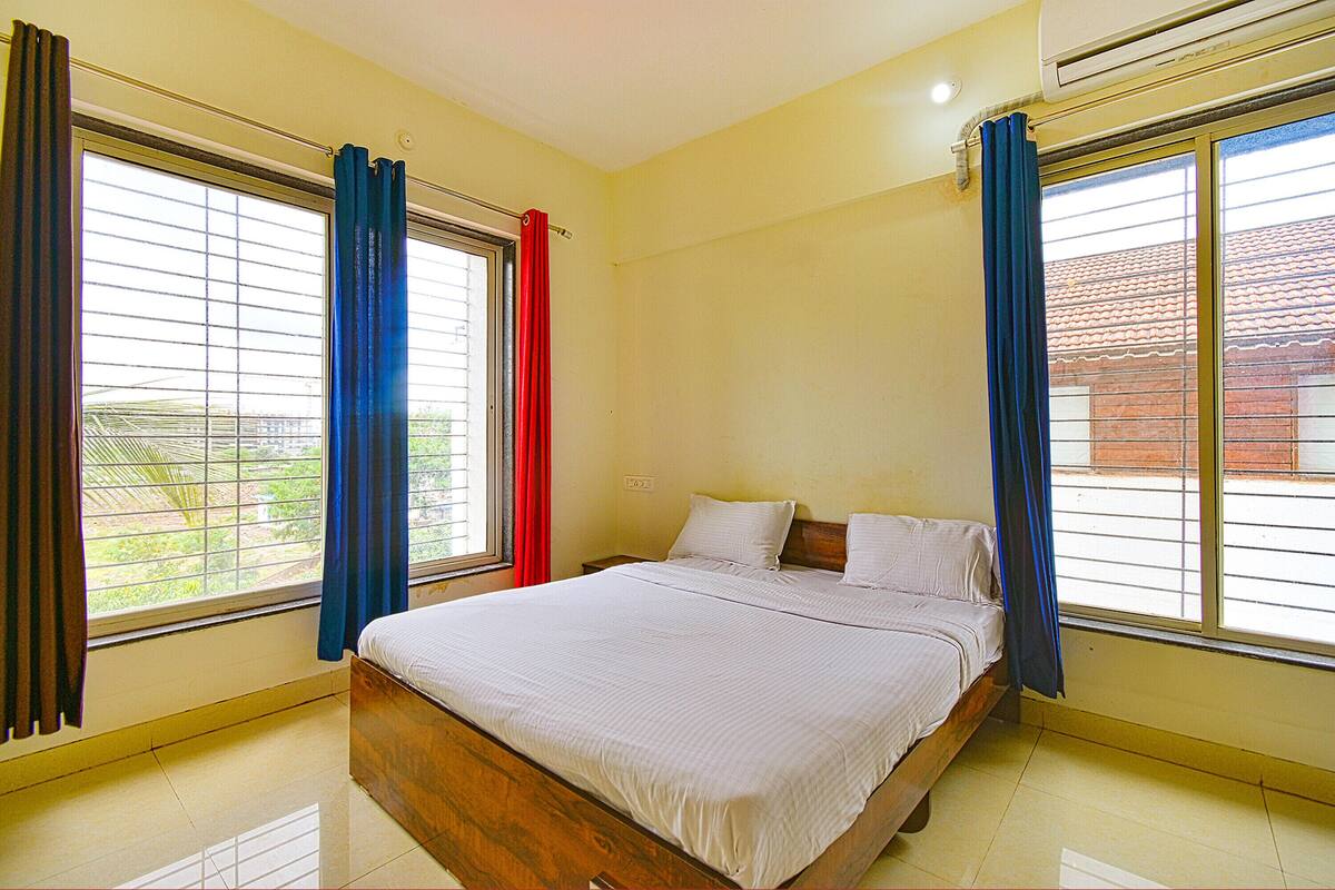 A bedroom with a bed, large windows with curtains, and an air conditioning unit.