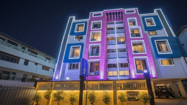 Un hotel de varios pisos con fachada moderna, luces de neón iluminadas y una entrada porticada con plantas en macetas.