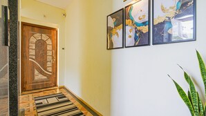 Un pasillo con una puerta de madera, una alfombra estampada y tres cuadros abstractos en la pared.