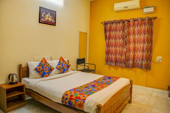 A bedroom with a bed, pillows, a nightstand, an air conditioner, and a mirror. - Fabhotel Hibiscus Stays (Chennai)