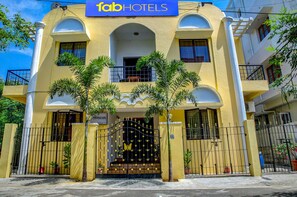 A yellow building with a sign reading "fab hotels" and a gated entrance with decorative elements. - Fabhotel Hibiscus Stays (Chennai)