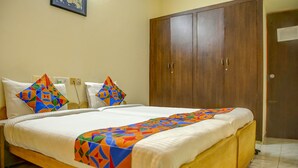 A neatly made bed with a colorful geometric-patterned throw, a wooden wardrobe, and a plain wall with a single framed picture. - Fabhotel Hibiscus Stays (Chennai)