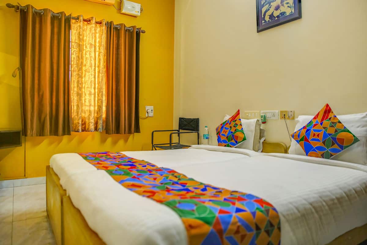 A hotel room with a bed, a chair, a small table, and a window with curtains.