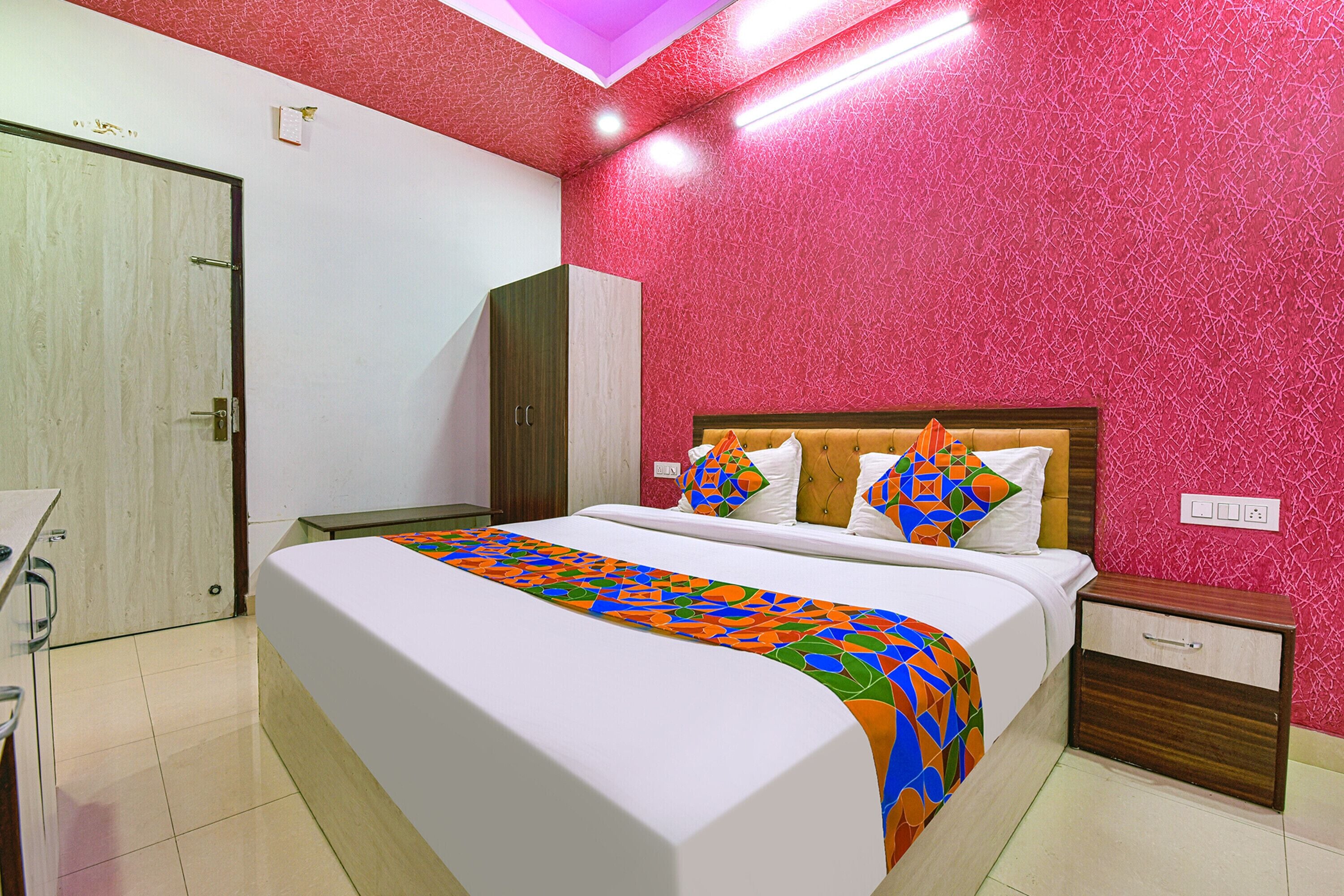 A hotel room with a large bed, a wooden wardrobe, a bedside table, and a red textured wall.