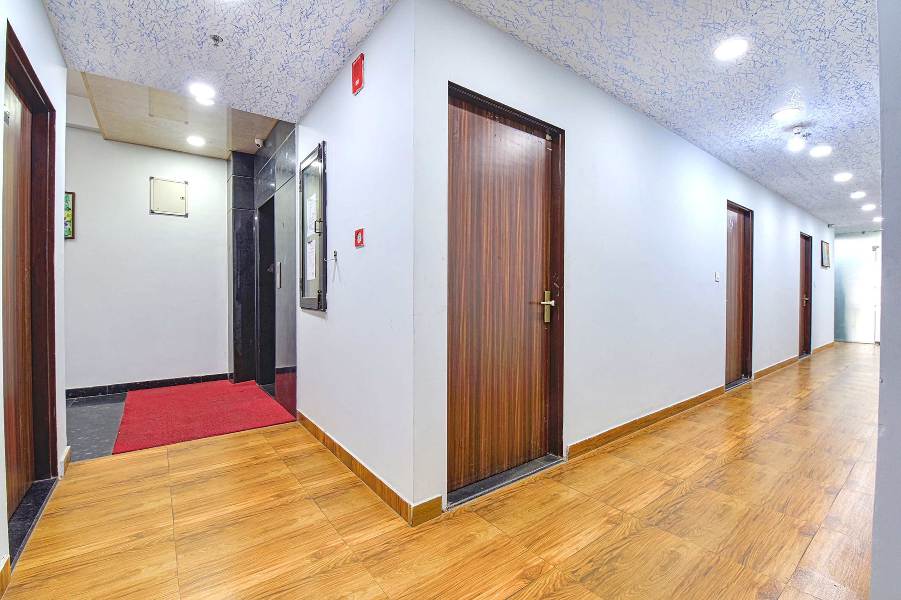 A hallway with wooden flooring, white walls, and a red carpet leading to a door.