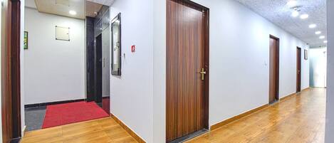 A hallway with wooden flooring, white walls, and a red carpet leading to a door.