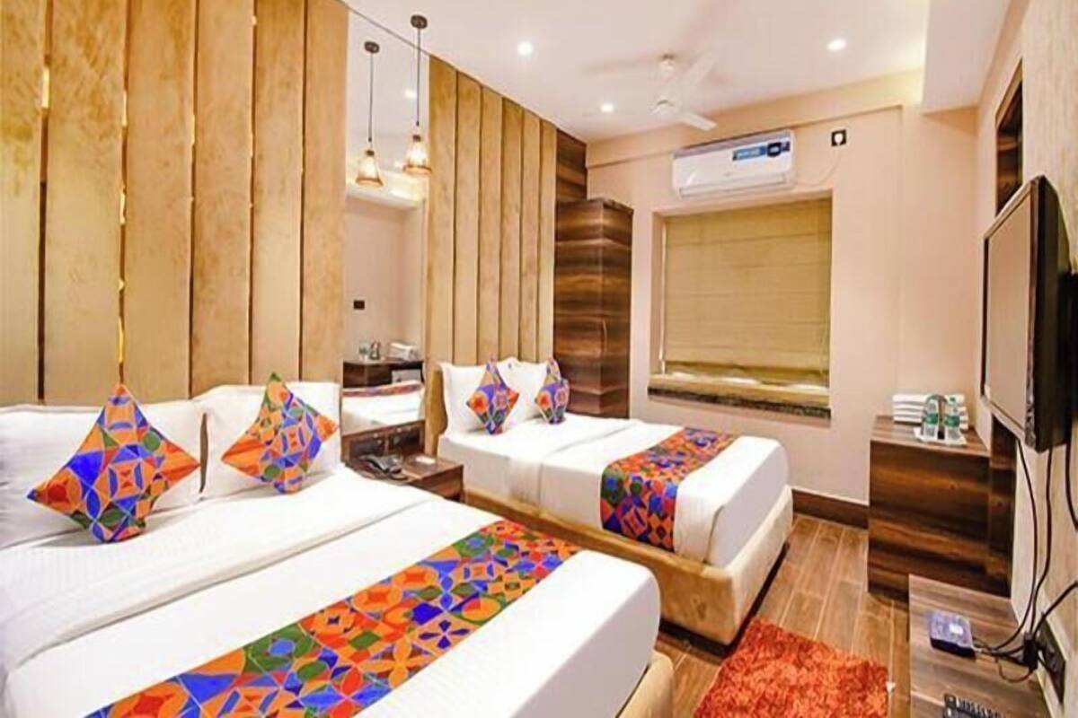 A hotel room with two beds, a TV, a window with blinds, and a ceiling fan.