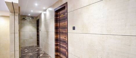 A hallway with a marble floor, a wooden door with a number plate, and a wall with a textured finish.