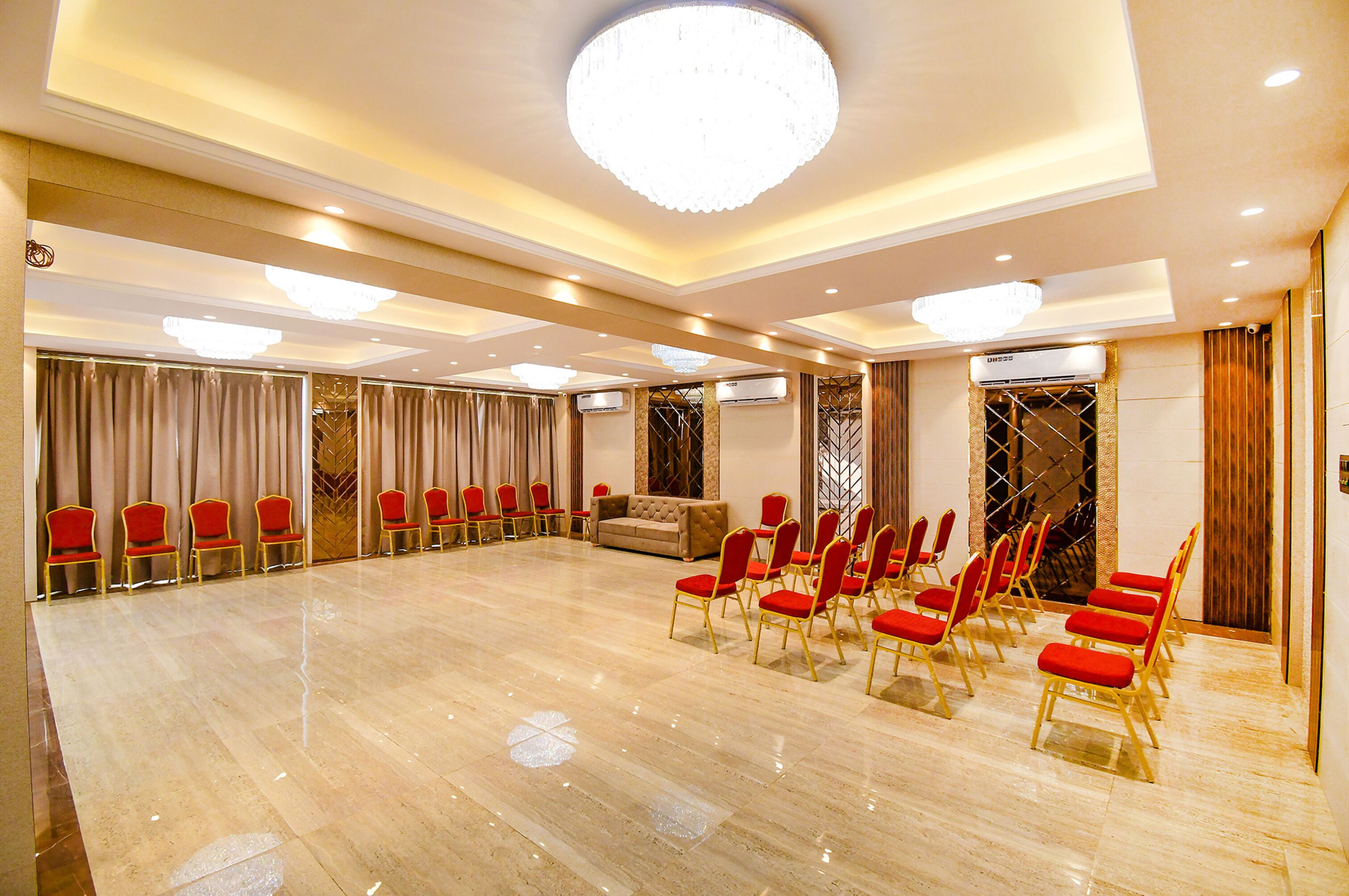Ein geräumiger Konferenzraum mit einem glänzenden Marmorboden, Reihen aus roten und goldenen Sesseln, einem komfortablen Sofa und einer großen Chandelier.