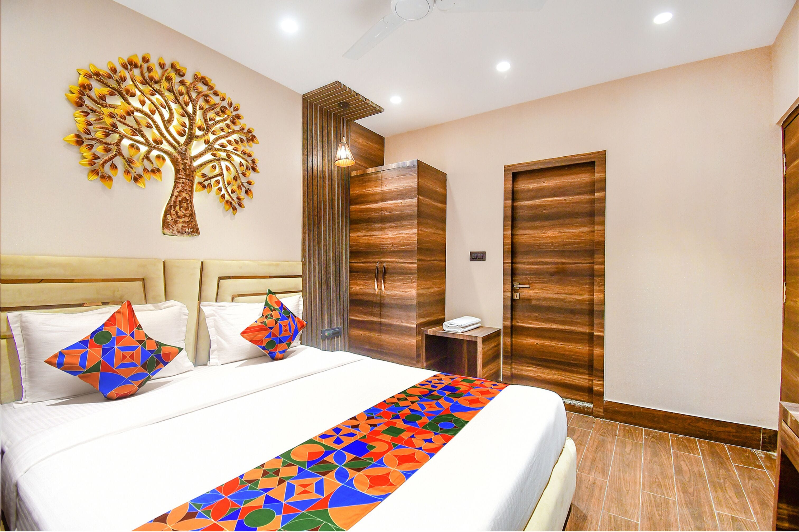 Ein modernes Hotelzimmer mit einem großen Bett, Wandkunst mit Baumdekor, einem Holzschrank und einem kleinen Nachttisch.