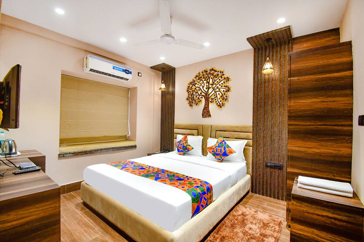 A hotel room with a bed, bedside table, air conditioning unit, window, and decorative wall art.