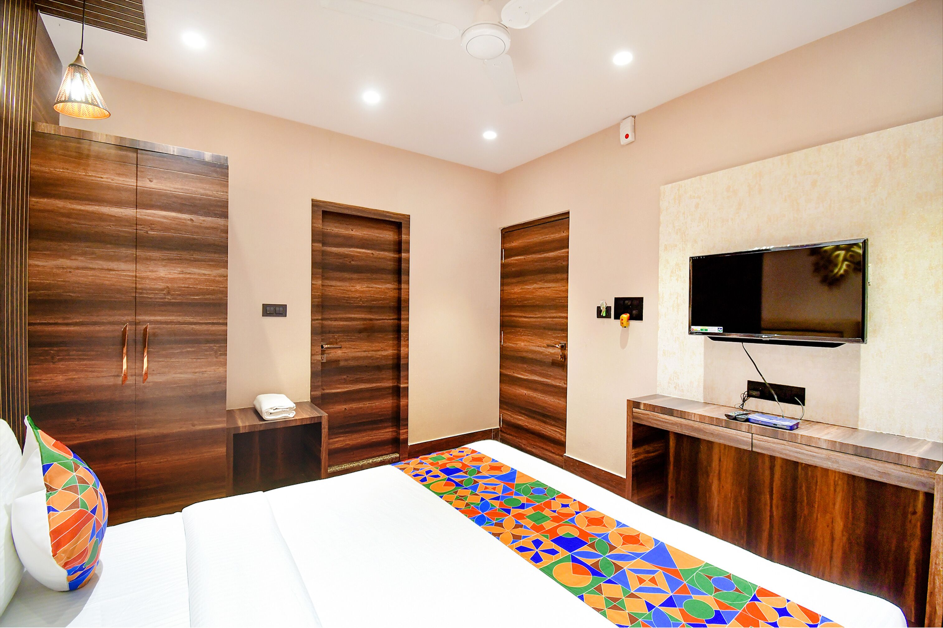 Une chambre d’hôtel avec un grand lit, une armoire en bois, un petit bureau et un téléviseur fixé au mur.