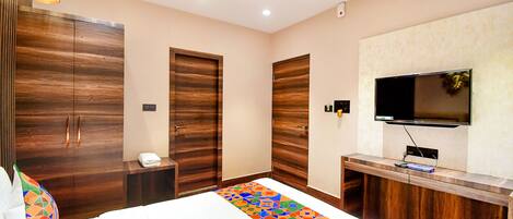 A hotel room with a large bed, wooden wardrobe, a small desk, and a television mounted on the wall.