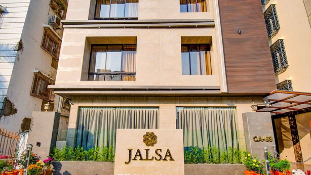 Ein Hotel Eingang mit einem Schild mit der Aufschrift 'JALSA', umgeben von Topfpflanzen und einem weißen Blumenbeet.