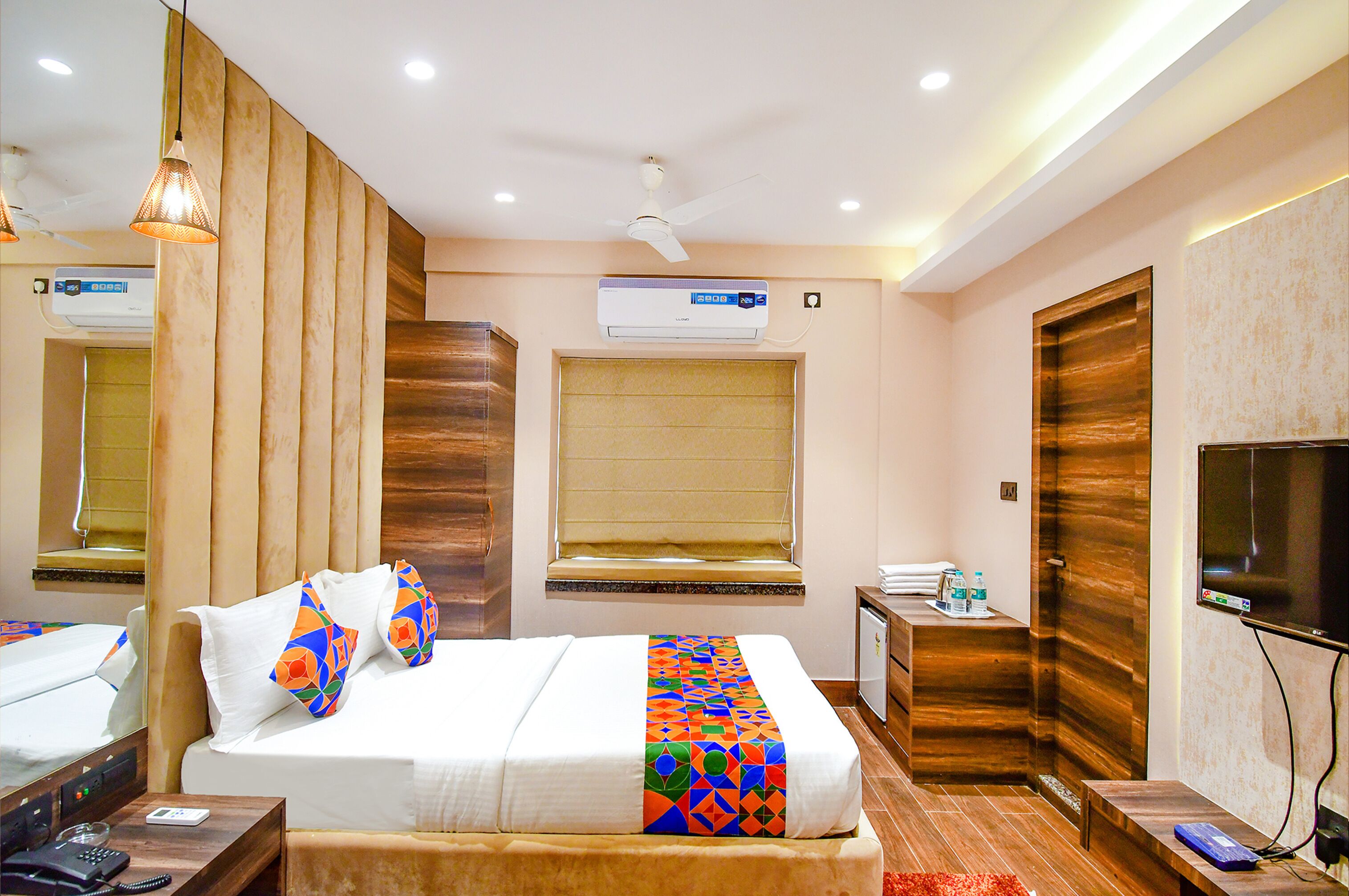Une chambre d’hôtel équipée d’un lit, d’une table de chevet, d’une commode, d’un téléviseur, d’un climatiseur, d’une fenêtre et d’un ventilateur de plafond.