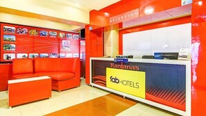 A reception area with a red couch, a reception desk, and a wall with various travel-related images. - Fabhotel Ranjanas (Paud)