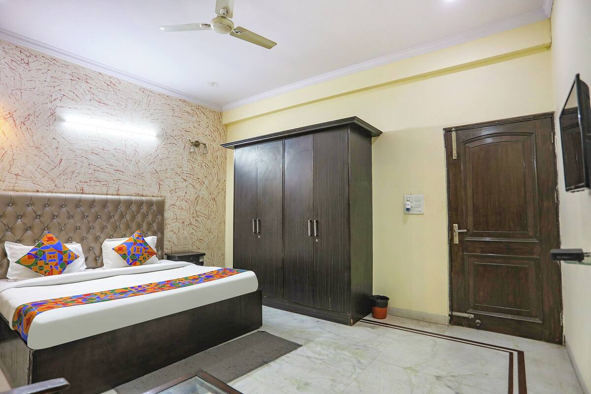 A bedroom with a tufted headboard, a bed with patterned pillows, a dark wardrobe, a door, and a ceiling fan.
