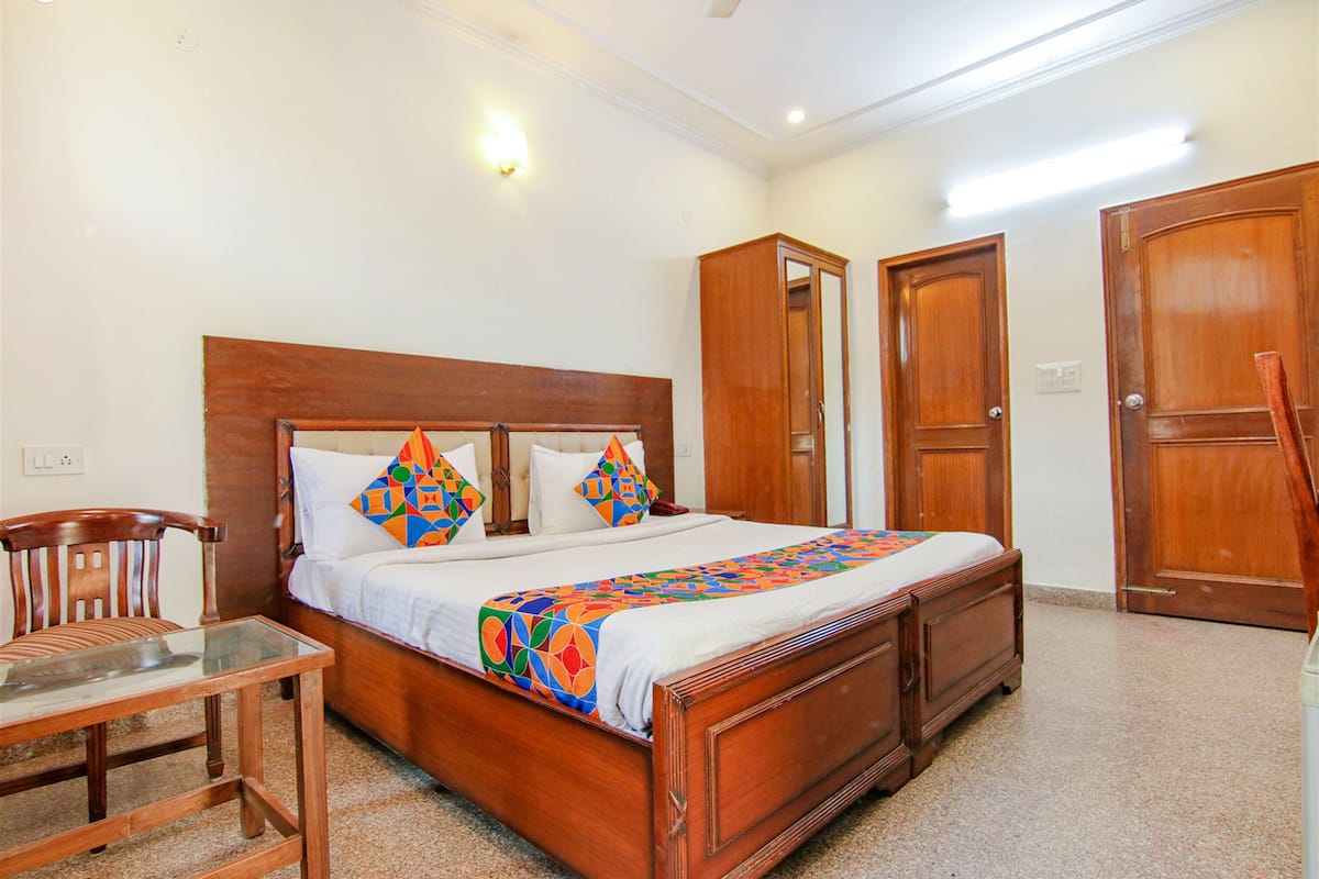 Une chambre spacieuse avec un grand lit, une armoire en bois, une table en verre et une chaise.