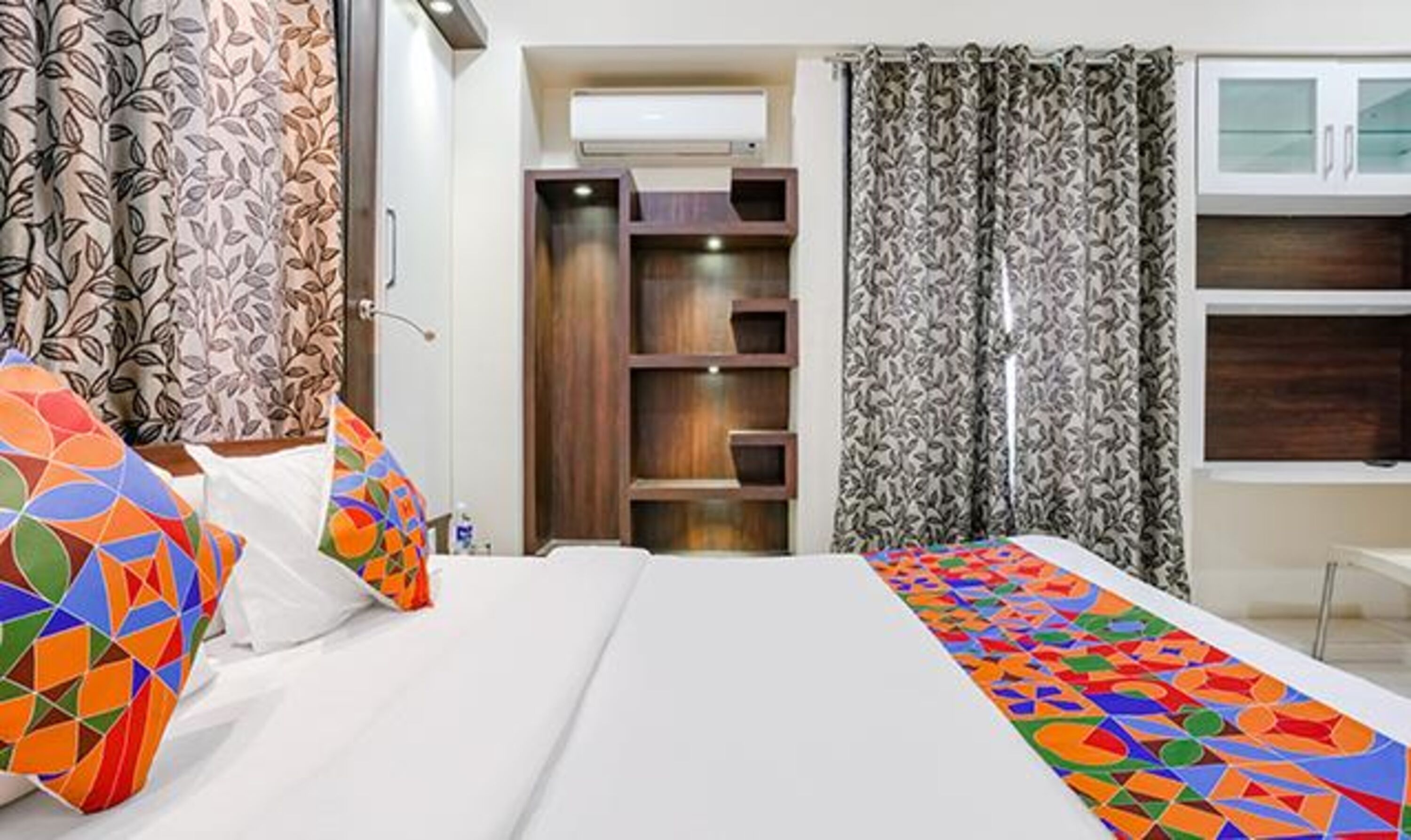 A hotel room with a bed, a wardrobe, a desk, and a window with curtains.
