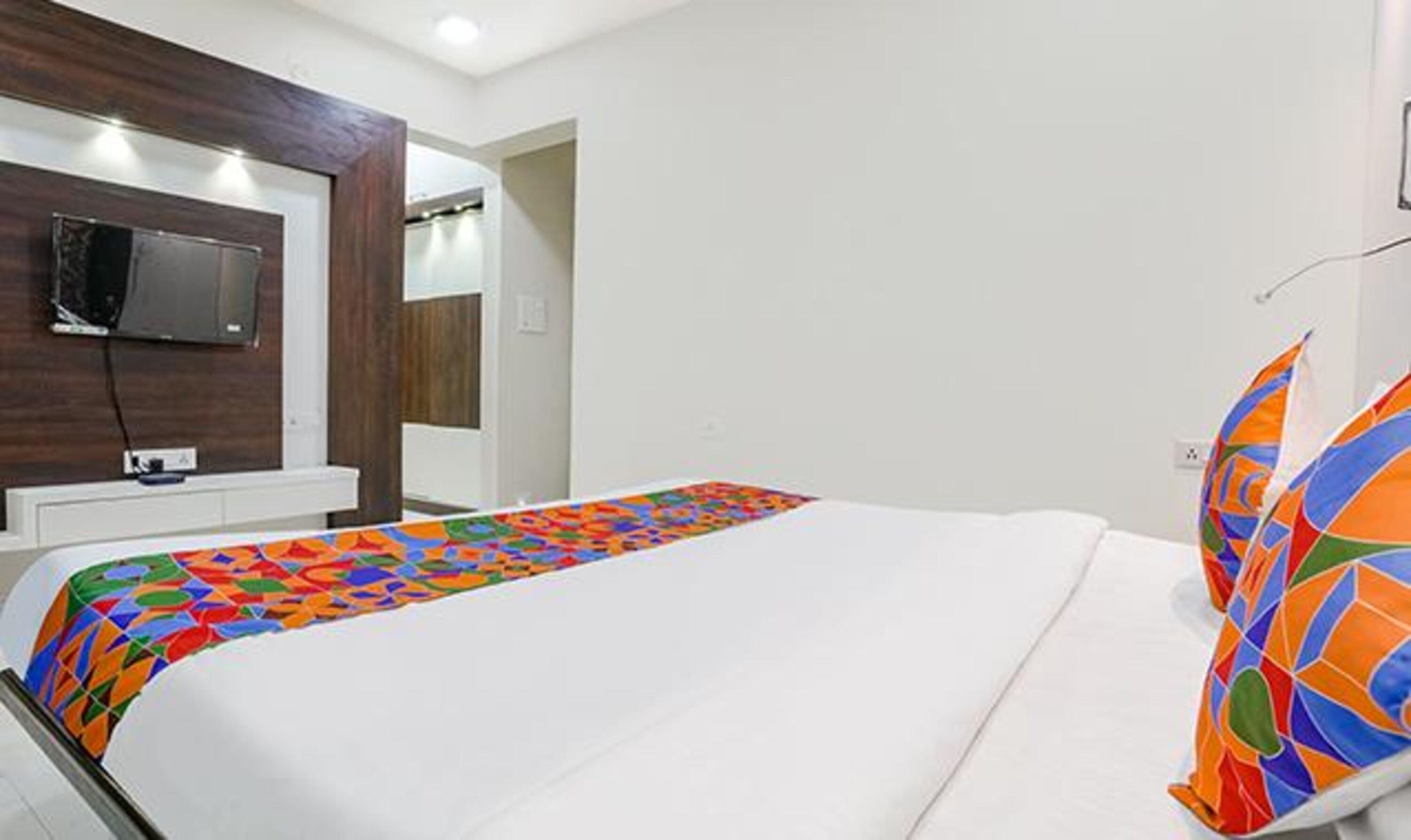 A hotel room with a bed, a TV mounted on the wall, and a colorful bedspread.