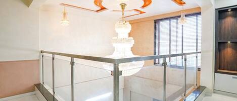 A spacious room with a high ceiling, a glass railing, and a chandelier.