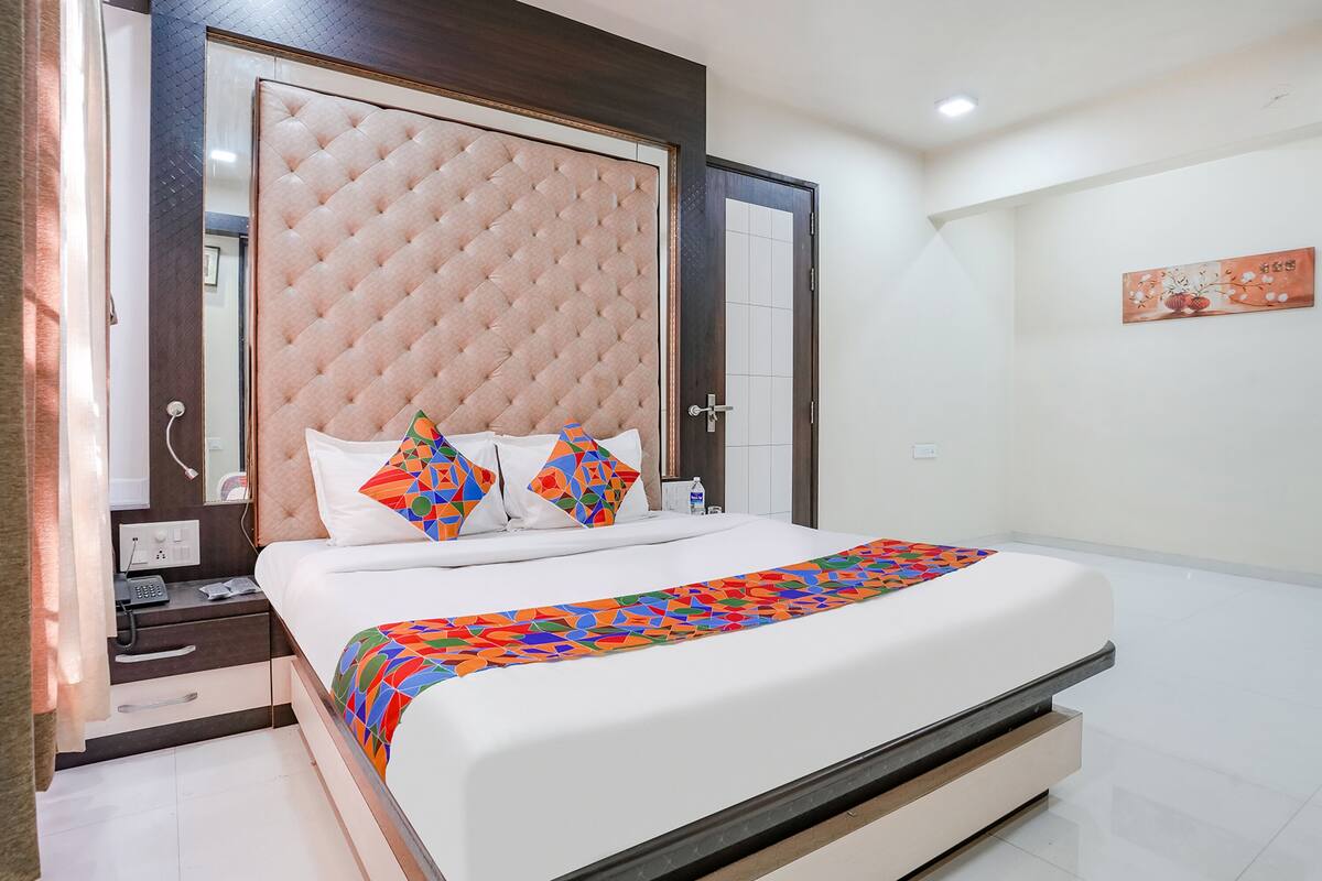 A neatly made bed with a colorful geometric-patterned blanket, a tufted headboard, and a bedside table with a phone and a bottle.