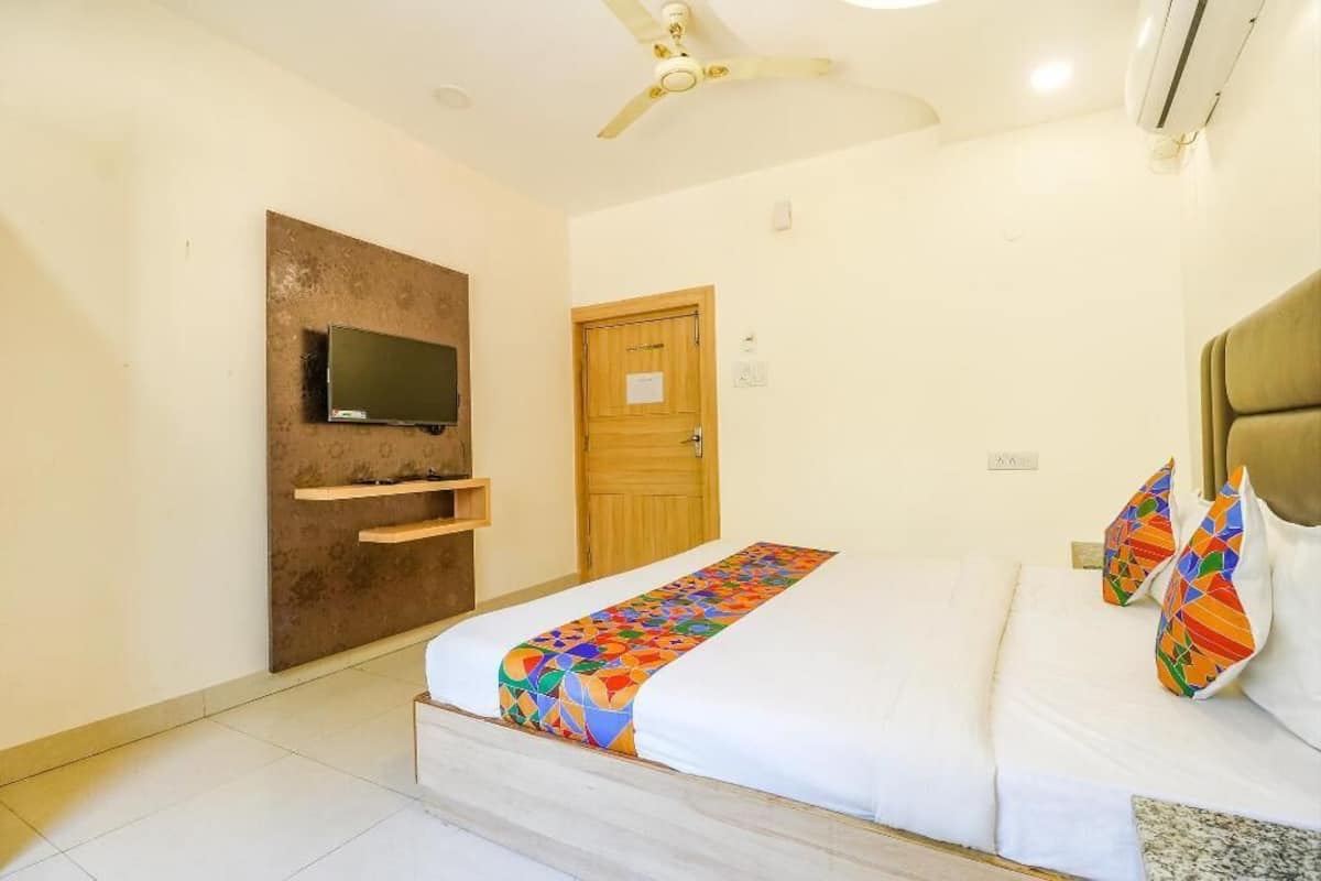 Quarto de hotel com cama, televisão fixada em um painel de madeira, ventilador de teto e ar condicionado.