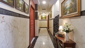 A hallway with marble walls, framed paintings, and a wooden bench with a vase of flowers. - Fabhotel Royal Aanandam (Gwalior)