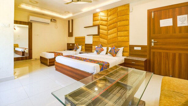 A hotel room with a large bed, a glass coffee table, a ceiling fan, and wooden paneling on the walls. - Fabhotel Royal Aanandam (Gwalior)